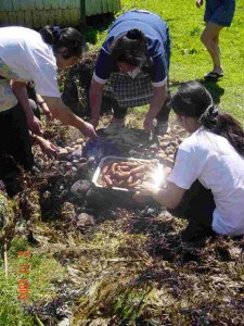These South American women are pulling sausages out from the middle layer while some potatoes cook on the top to one side.